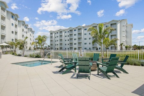 A pool surrounded by green chairs and palm trees.