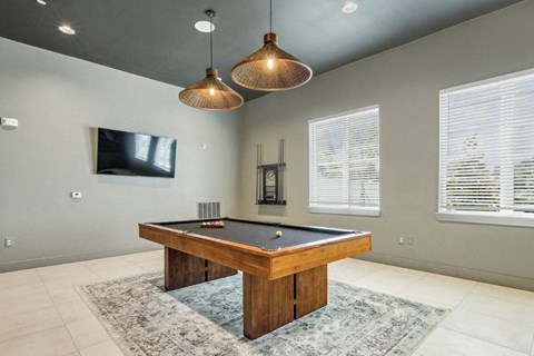 A pool table in a room with a television and windows.