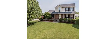 A house with a large lawn and a tree in front.