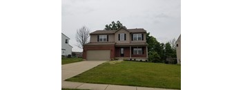 A two-story house with a garage is surrounded by a green lawn.