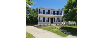 A two-story house with a front porch and a stone wall.