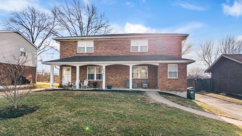 A house with a brick facade and a green trash can in front.