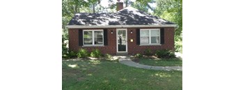 A small brick house with a black roof and a white door.