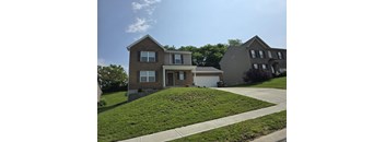 A house with a brown roof and a grey wall is surrounded by a green lawn.