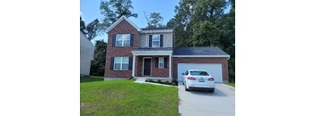 A white car is parked in front of a brick house.