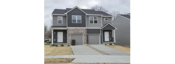 A grey house with a white door and a brown trash can.