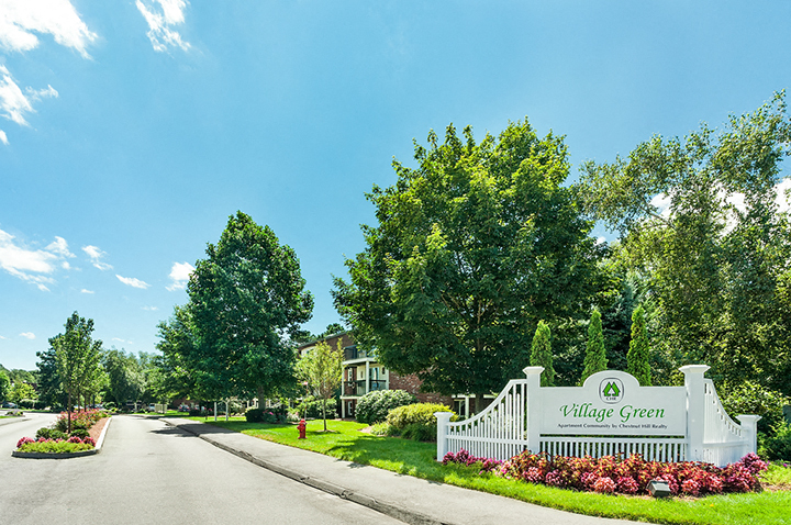 A sign that says "Village Green" stands in front of a white fence.