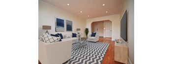 A living room with a white couch, a black and white rug, and a flat screen TV mounted on the wall.