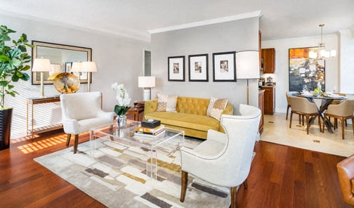 A living room with a white sofa, a glass coffee table, and a rug with a pattern of squares.