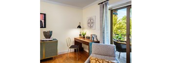 A room with a desk, chair, and a cabinet with a vase on top.