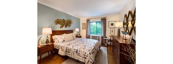 A bedroom with a patterned bedspread and a wooden dresser.