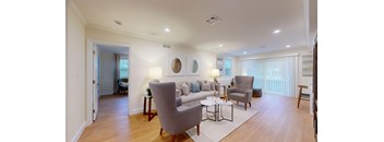 A living room with a grey couch, a grey armchair, a white sofa, a white coffee table, a white rug, a white wall, a white ceiling, a white door, a white chair, a white table,