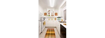A kitchen with white cabinets and a checkered rug on the floor.
