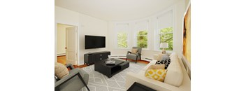 A living room with a white couch, a black coffee table, and a flat screen TV mounted on the wall.