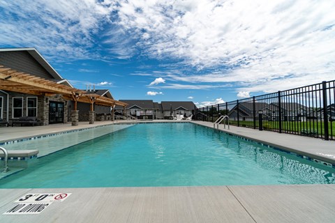 A large outdoor swimming pool with a wooden deck and a black fence.
