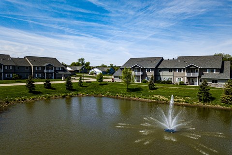 A fountain in the middle of a pond in front of apartment buildings.
