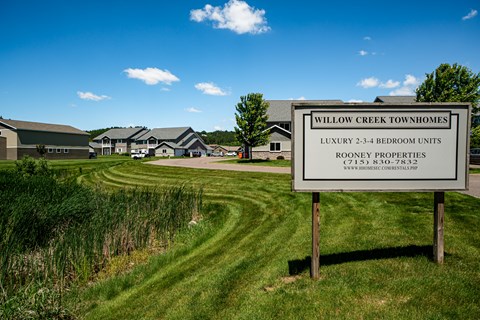 A sign for Willow Creek Townhomes is in front of a grassy area.