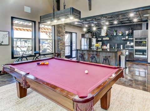 A pool table in a room with a kitchen in the background.