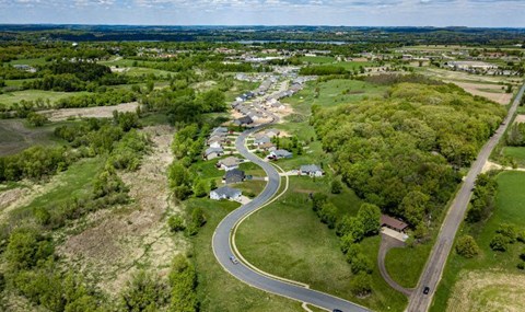 A road curves through a green landscape with a few buildings.