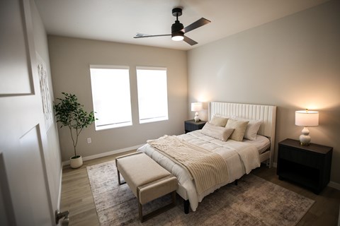A bedroom with a large bed, a ceiling fan, and a potted plant.