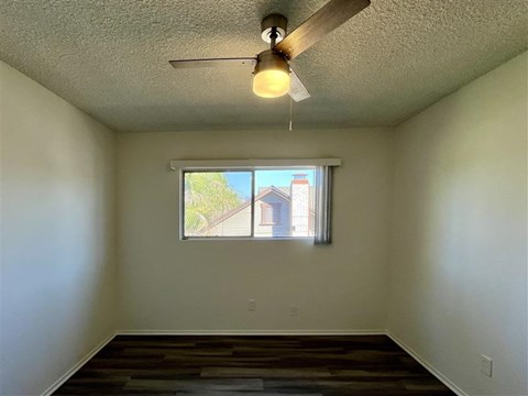 A room with a ceiling fan and a window showing a house outside.