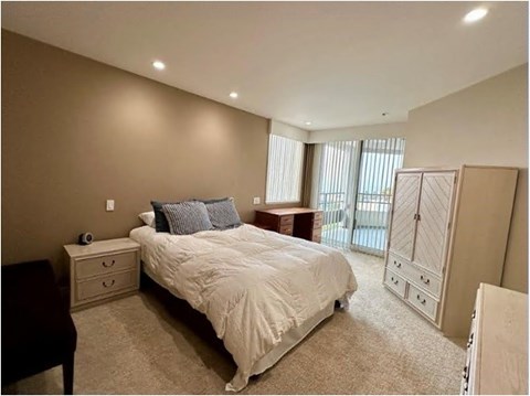 A bedroom with a large bed, nightstand, and a window with blinds.