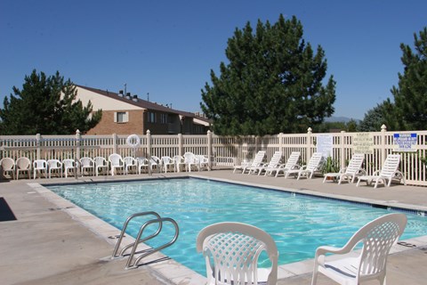 A pool with chairs around it and a building in the background.