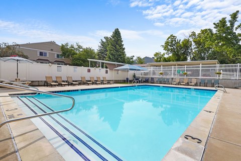 A large outdoor swimming pool with a blue tiled edge and a white fence surrounding it.