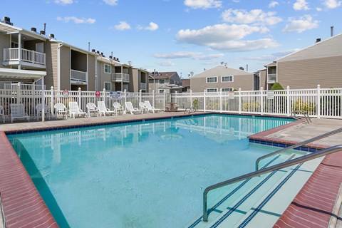 A swimming pool surrounded by a white fence and chairs.