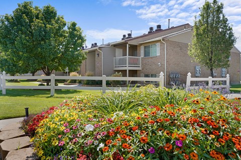 A flower bed in front of a building with a white fence.