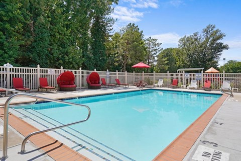 A swimming pool surrounded by trees and red chairs.