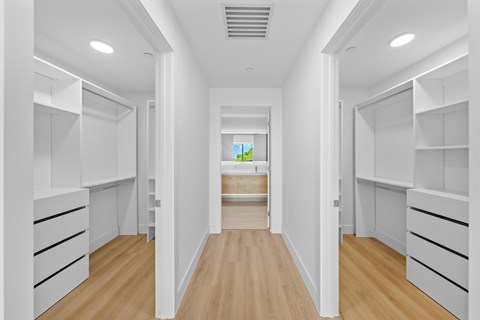 A long hallway with white shelves on the side and a view of a green field through a window.