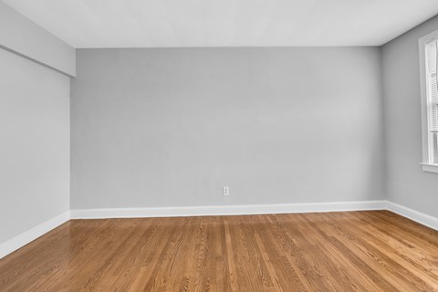 A room with wooden flooring and a window on the right side.