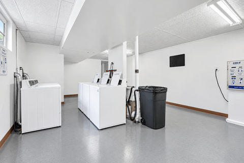 A clean, empty room with white appliances and a black trash can.