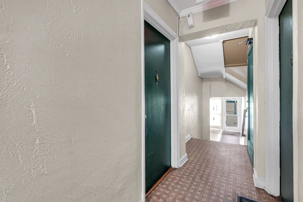 an empty hallway with a green door and a kitchen in the distance