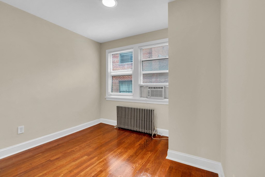 a living room with wood floors and a radiator and two windows