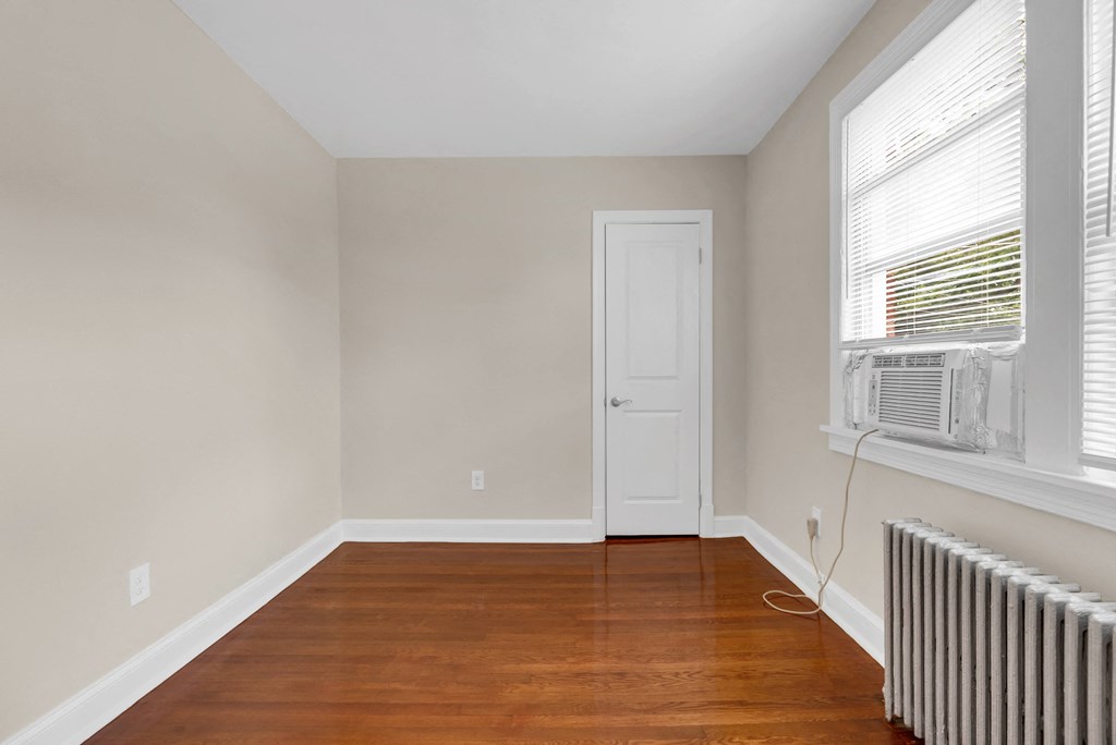 an empty room with wood floors and a radiator and a white door