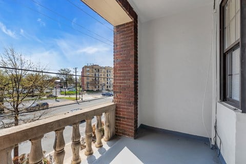 A balcony with a brick pillar and concrete floor overlooks a street.