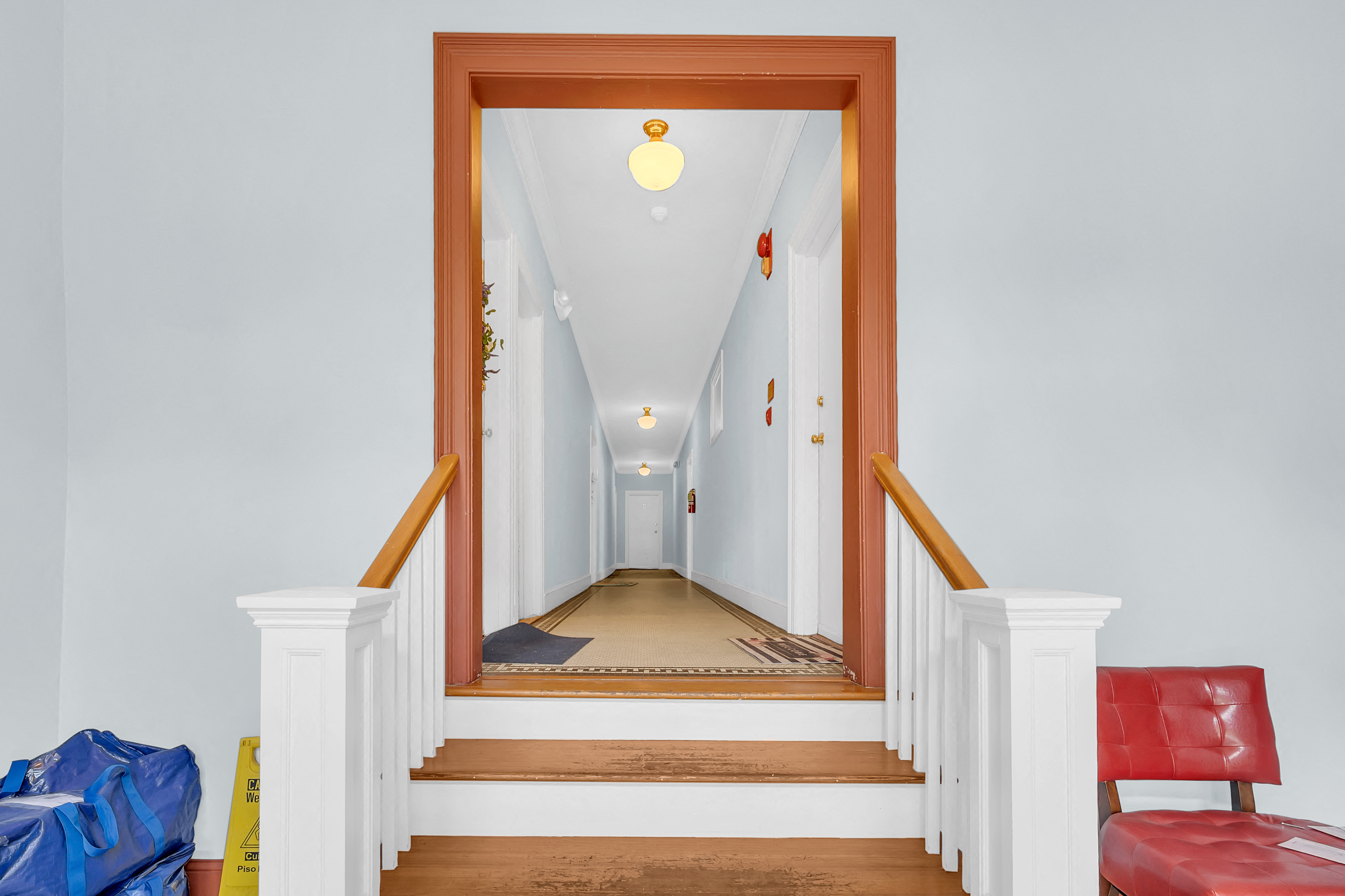 A hallway with a red chair and a blue bag on the floor.