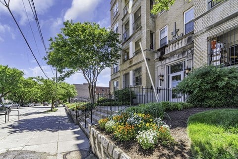 a sidewalk in front of a building with trees and flowers