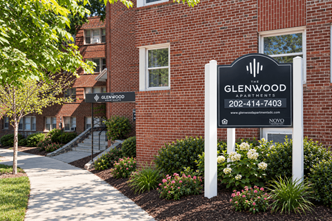 A sign for Glenwood Apartments is displayed in front of a brick building.