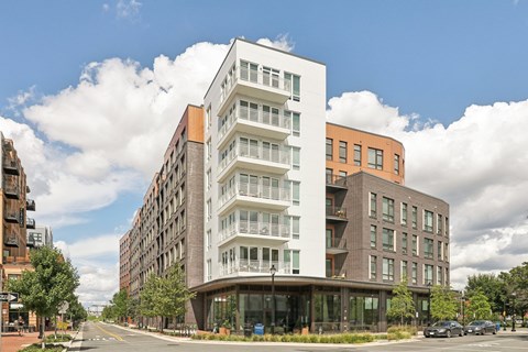 A modern multi-story building with a white and brown facade is situated on a street corner with cars parked in front.