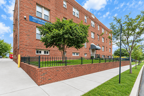 A red brick building with a black fence and a tree in front.