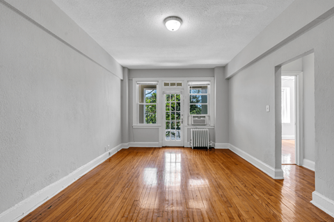 an empty living room with wood floors and a door to a balcony