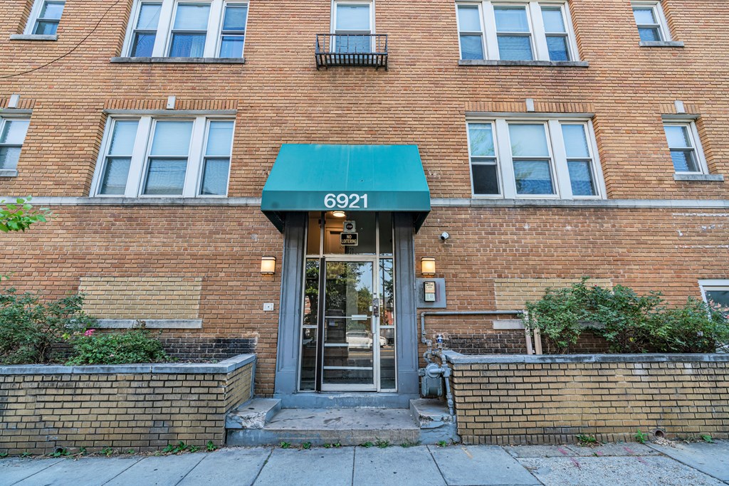 the front of a brick building with a green awning and a glass door