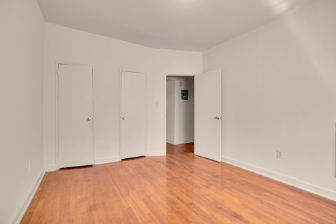 A room with wood floors and white walls with three doors and one open.