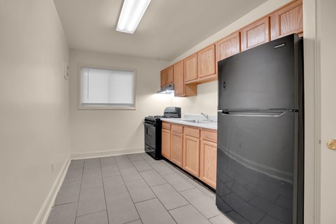A kitchen with a black refrigerator, wooden cabinets, and a window.