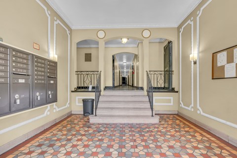 A hallway with a tiled floor and a series of mailboxes on the wall.