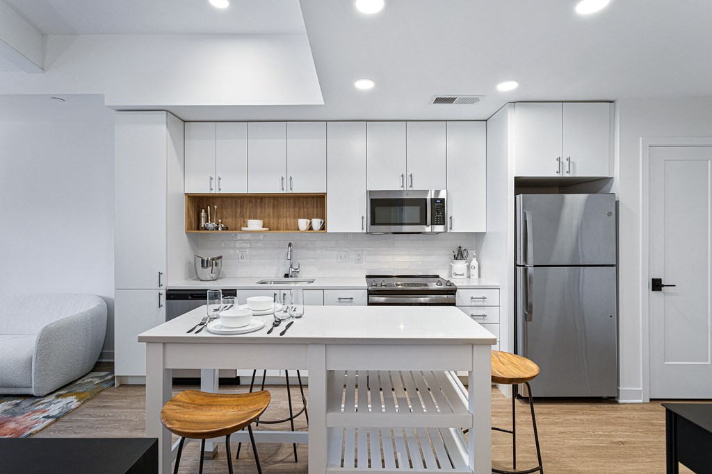 a white kitchen with a white island and a stainless steel refrigerator