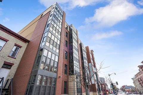 A tall red brick building with many windows is in the middle of a city street.